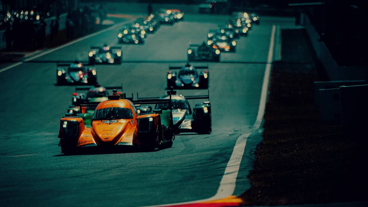 Grupa samochod&oacute;w wyścigowych klasy LMP2 ścigających się na torze w nocy.