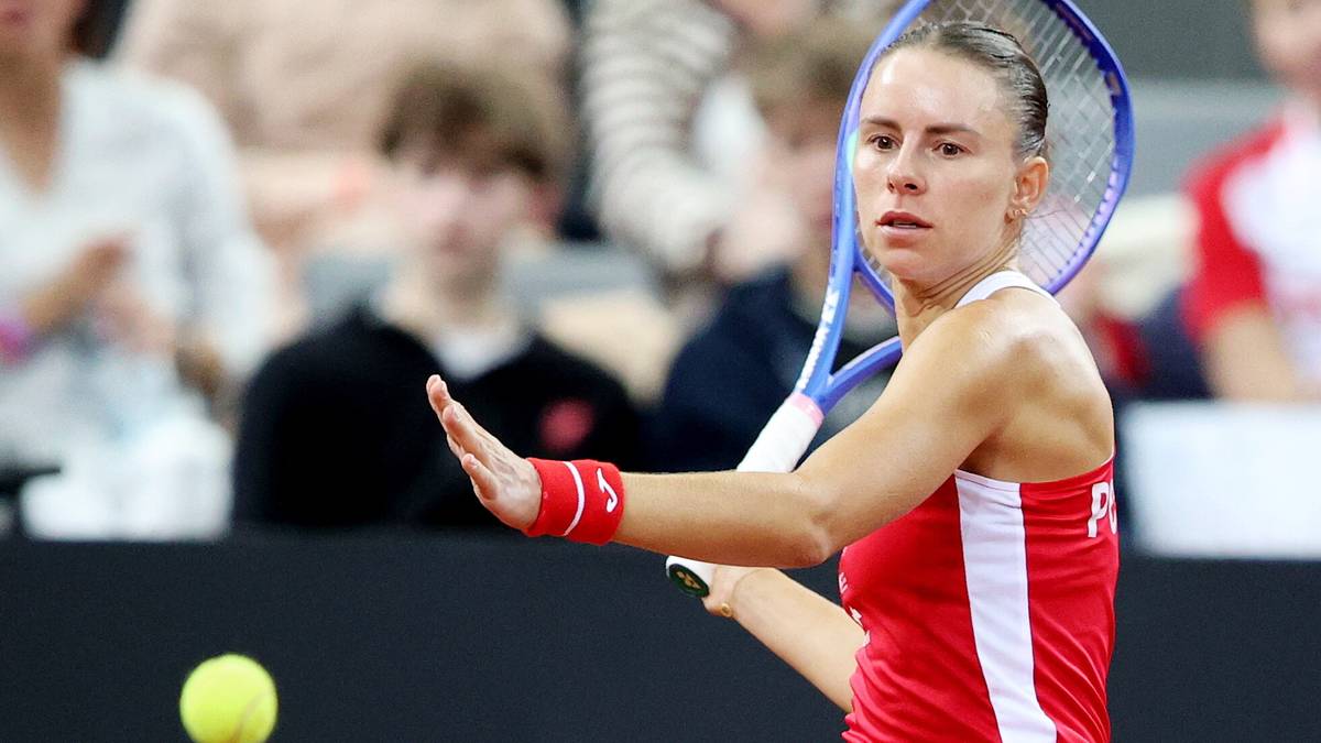 Tenisistka w czerwonej koszulce z rakietą w dłoni podczas meczu, skupiona na piłce.