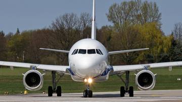 Przód białego samolotu Airbus A320 stojącego na płycie lotniska, z widocznymi światłami nawigacyjnymi i turbinami silników.