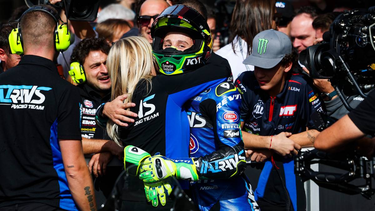 Motocyklista w kasku i stroju wyścigowym świętuje w otoczeniu tłumu.