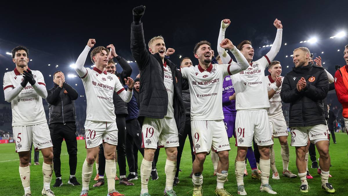 Piłkarze Widzewa Ł&oacute;dź w białych strojach z czerwonymi detalami świętują na murawie stadionu.