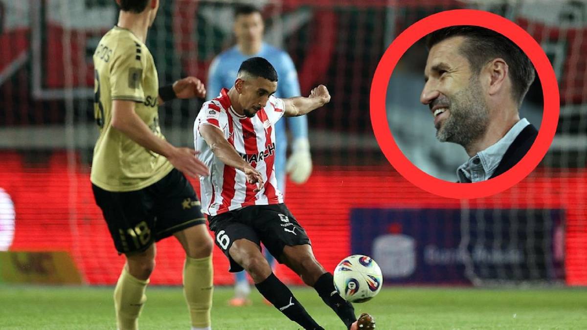 Dwóch piłkarzy na boisku, jeden z nich oddaje strzał na bramkę. W prawym górnym rogu kadru, w czerwonym okręgu, znajduje się zbliżenie twarzy trenera.