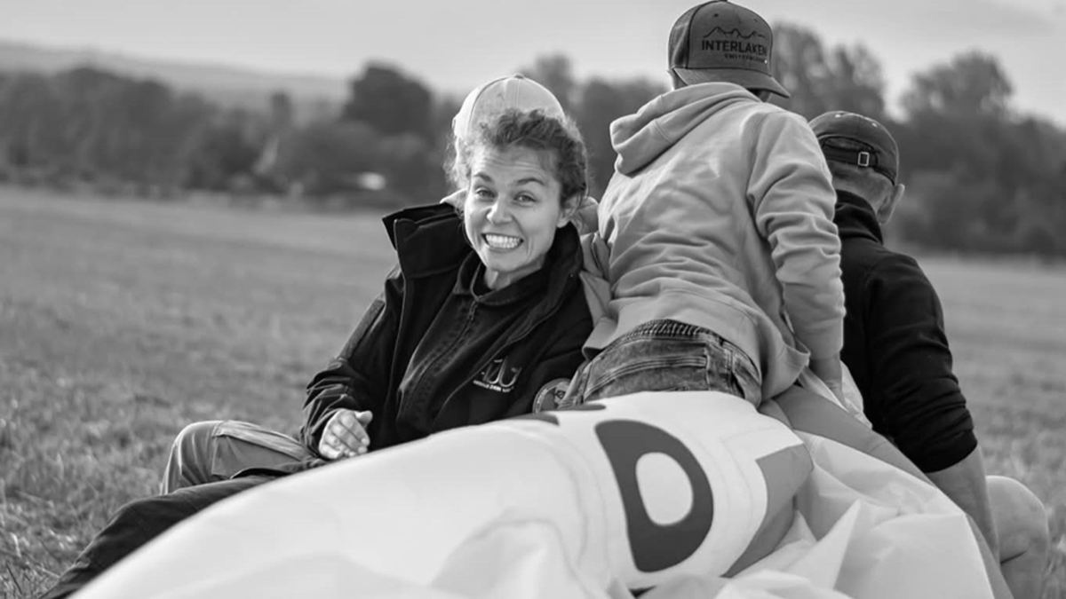 Trzy osoby siedzące na ziemi obok dużego, złożonego balonu.