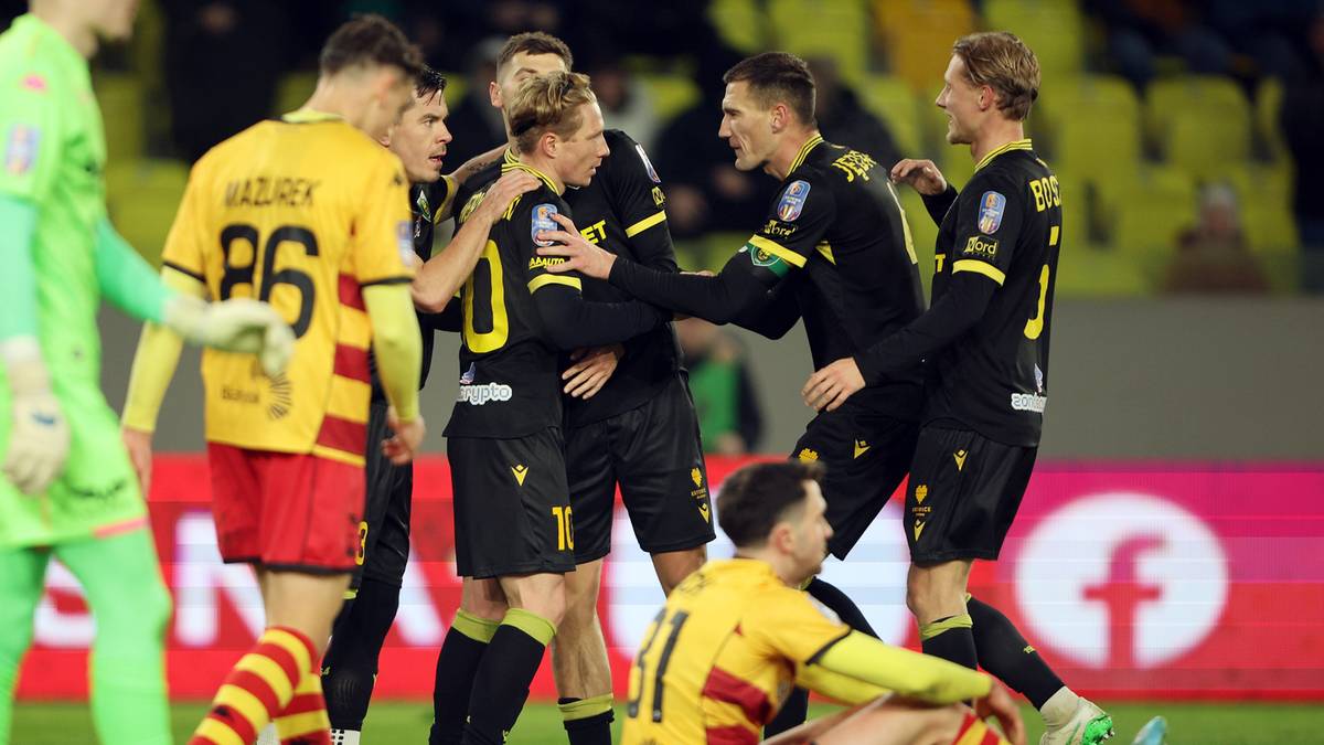 Piłkarze w czarnych strojach celebracji zdobytej bramki, jeden klęczy na boisku.