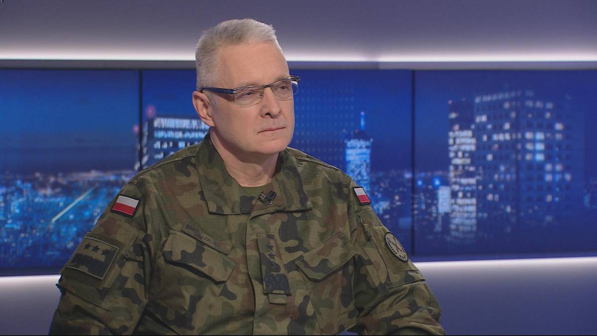 Mężczyzna w mundurze wojskowym siedzi przed ekranami wyświetlającymi nocną panoramę miasta.