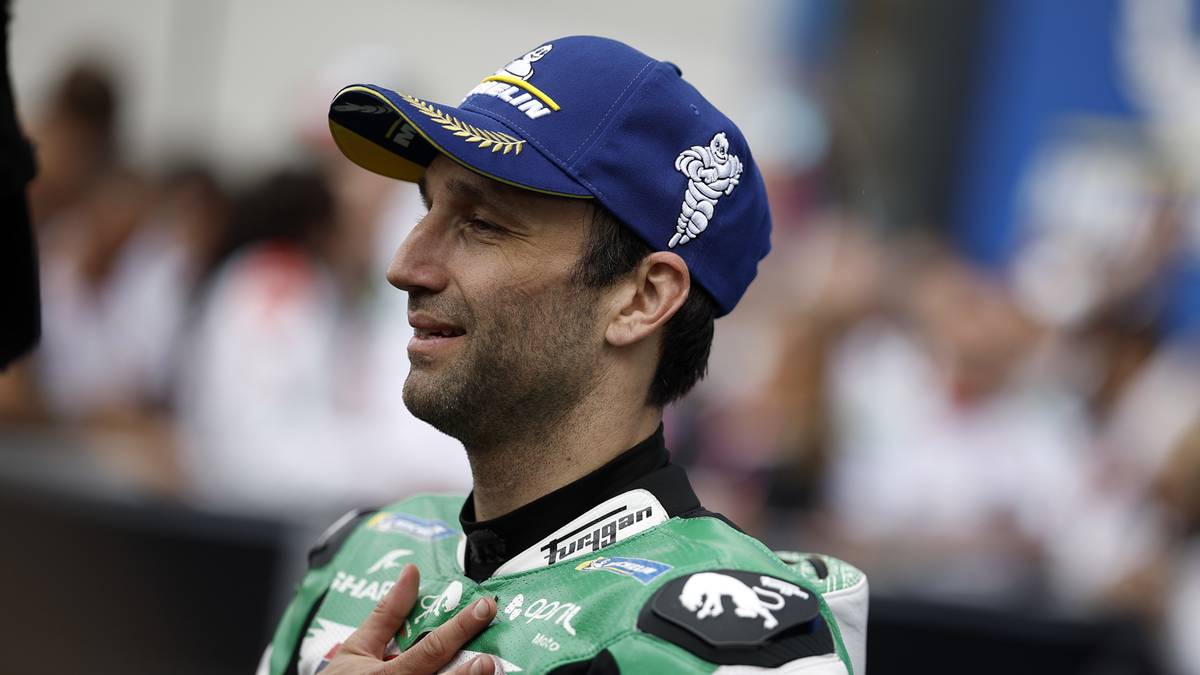 Mężczyzna w niebieskiej czapce z daszkiem Michelin i zielonym kombinezonie motocyklowym z białymi akcentami, patrzący w bok z wyrazem koncentracji na twarzy.