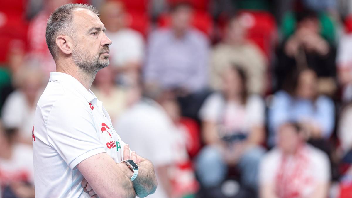 Mężczyzna w białej koszulce reprezentacji Polski z założonymi rękami, patrzący w bok.