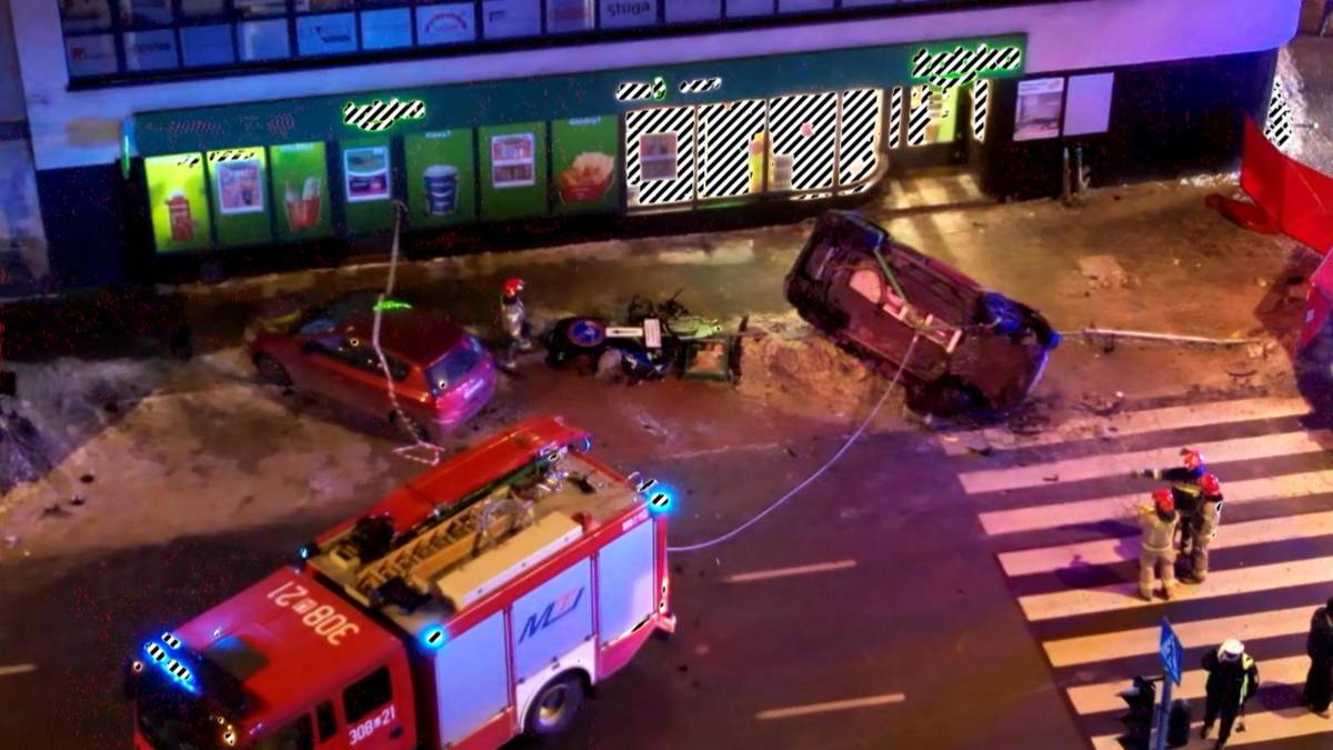 Miejsce wypadku drogowego z przewr&oacute;conym na dach samochodem, wozem strażackim i ratownikami.