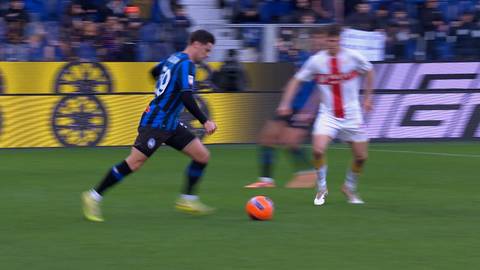 Piłkarz w czarno-niebieskim stroju prowadzi piłkę na boisku, podczas gdy przeciwnik w białym stroju stara się go zatrzymać.