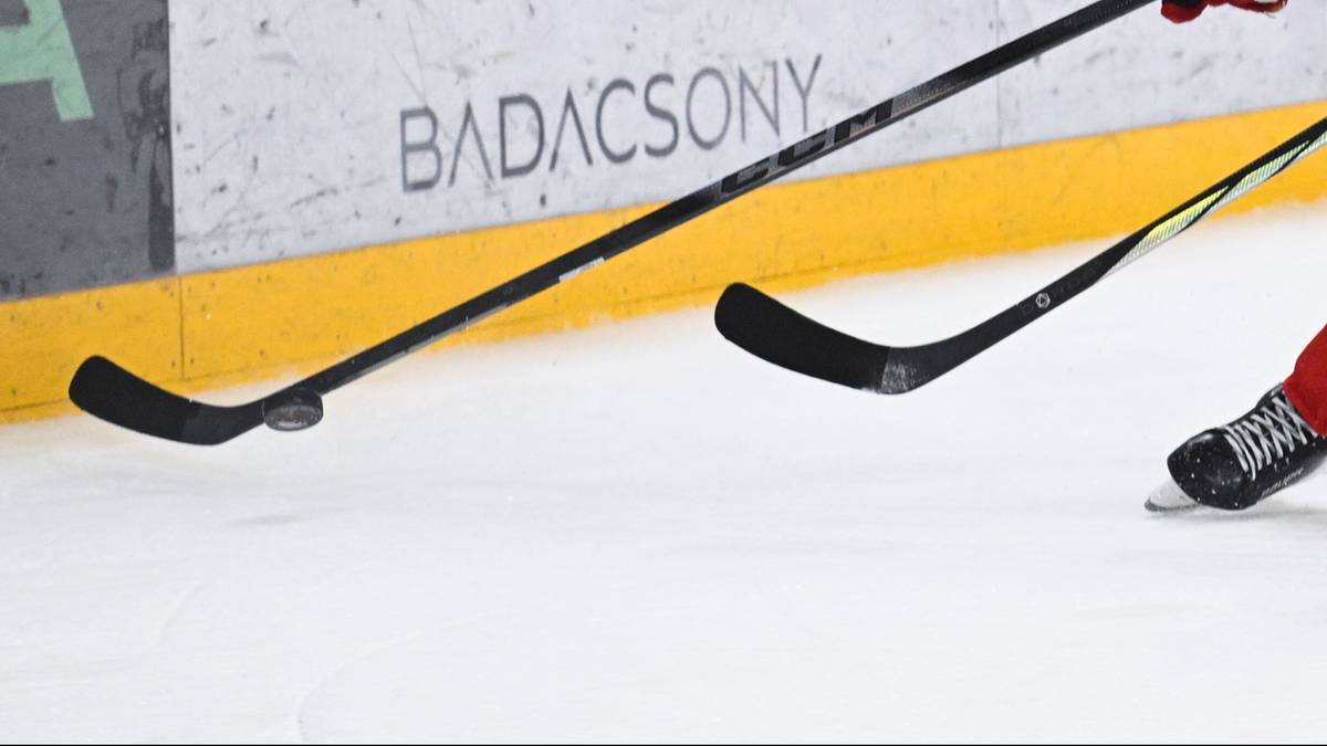 Dwóch hokeistów w czerwonych i białych strojach walczy o krążek na lodowisku.