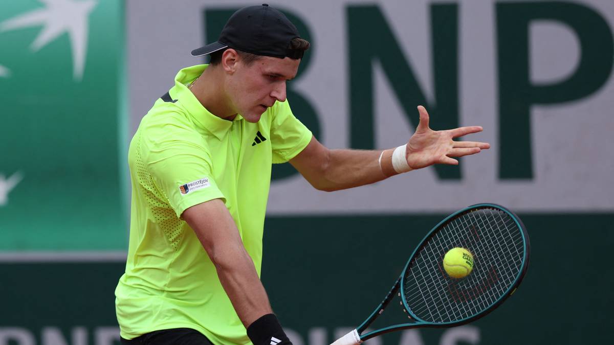 Tenisista w żółtej koszulce wykonuje uderzenie rakietą podczas meczu.