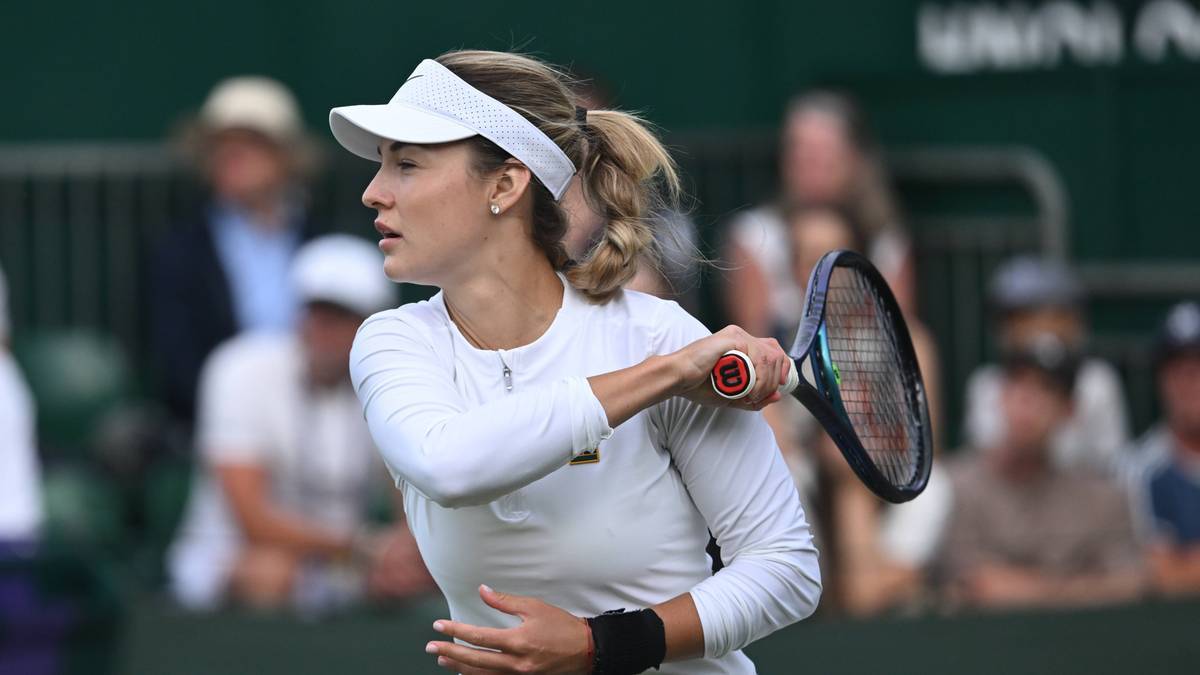 Kobieta tenisistka w białym stroju, patrząca w bok, z rakietą w ręku, podczas meczu.