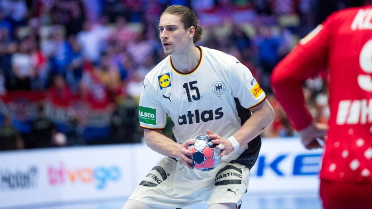 Piłkarz ręczny w białej koszulce z numerem 15 trzyma piłkę w rękach.