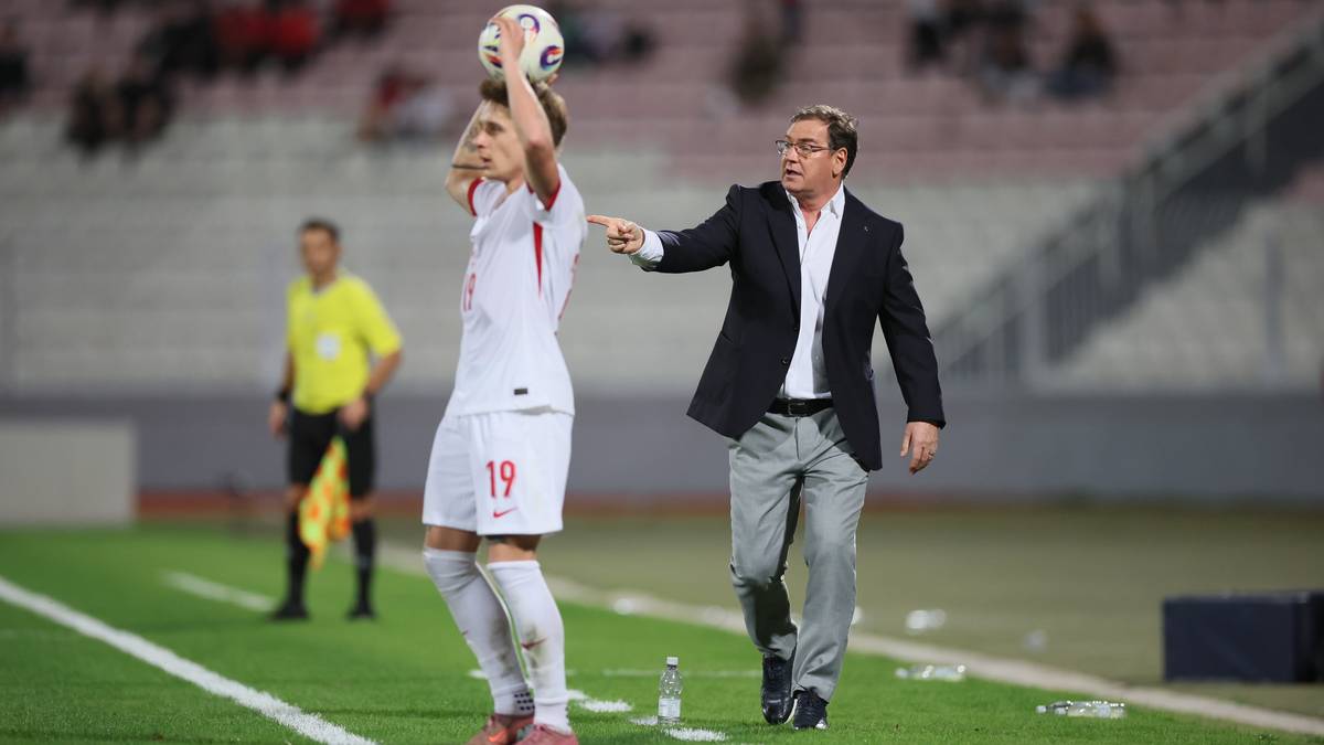 Piłkarz z piłką nad głową i trener wskazujący palcem na boisku.