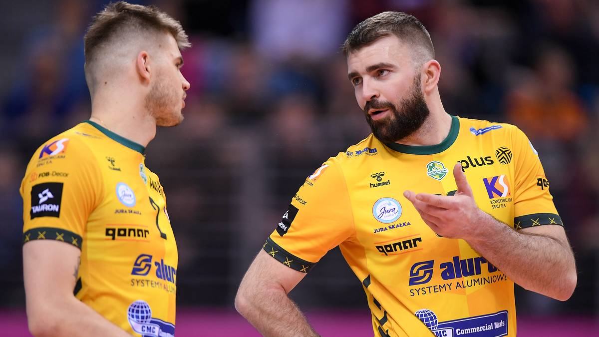Dw&oacute;ch siatkarzy w ż&oacute;łtych strojach sportowych rozmawia ze sobą na siatkarskim boisku.