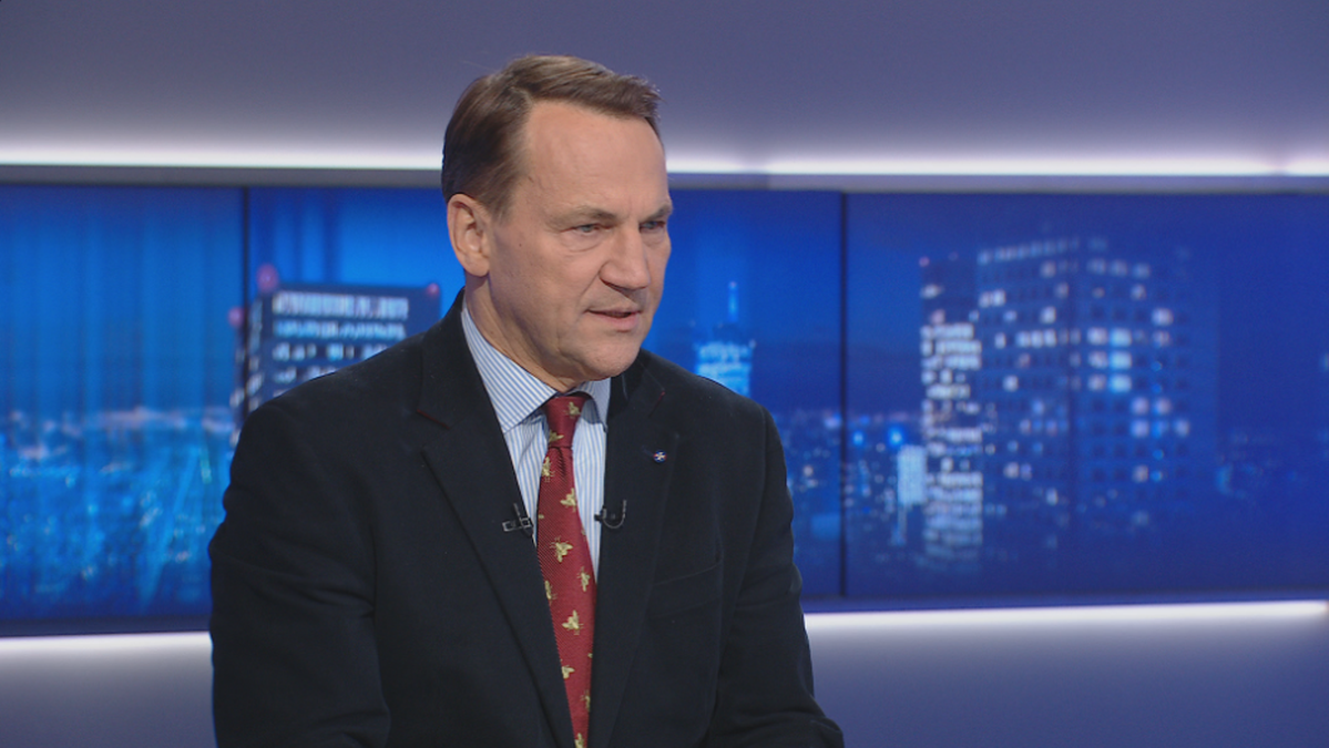 Mężczyzna w garniturze i krawacie udziela wywiadu w studiu telewizyjnym.