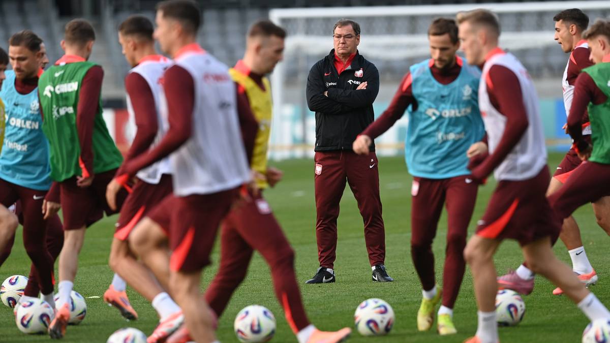 Trener siedzący na ławce rezerwowych podczas meczu piłki nożnej, otoczony przez zawodników w bordowych strojach.