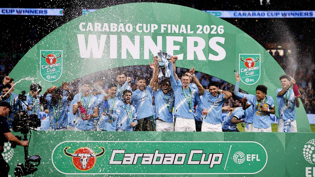 Drużyna Manchesteru City świętuje zdobycie Pucharu Ligi, wznosząc trofeum na tle zielonej scenografii z logo zawod&oacute;w.