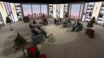 Grupa os&oacute;b siedzi w okręgu na kanapach i fotelach w studiu telewizyjnym. W tle znajdują się regały z dekoracjami świątecznymi.