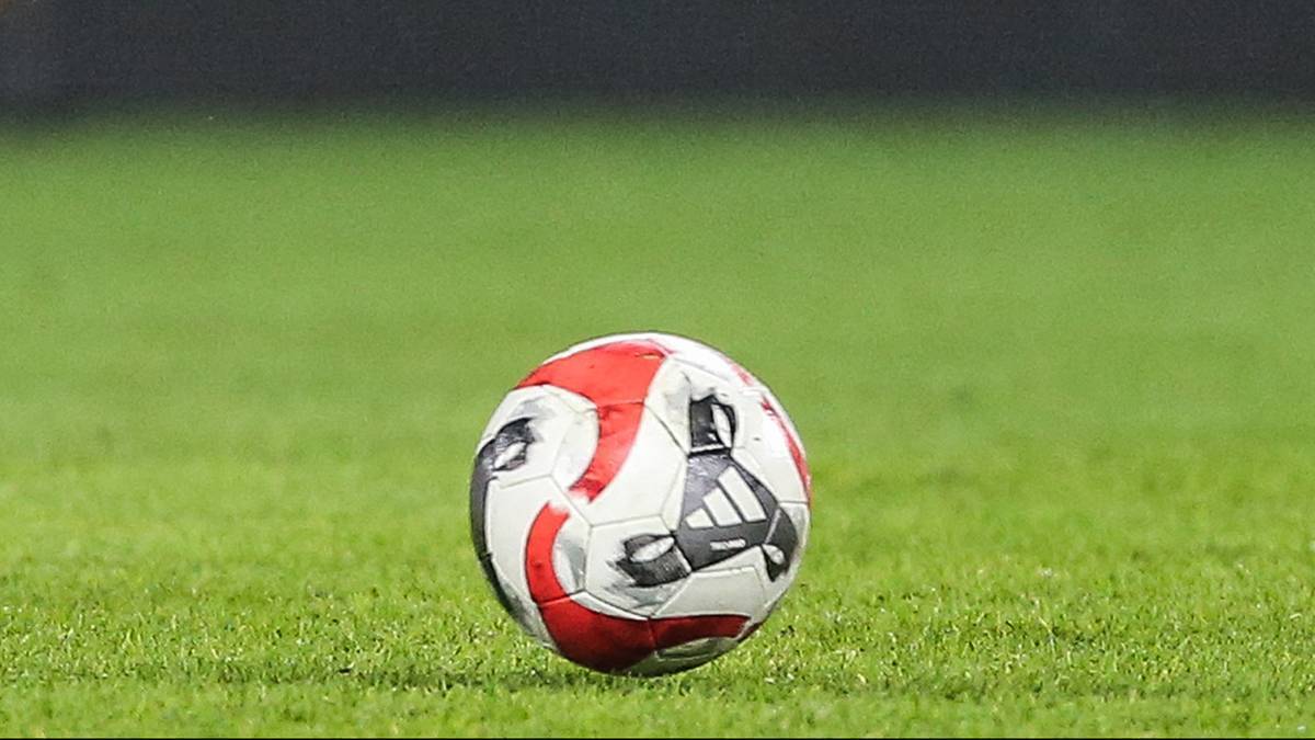 Piłka do piłki nożnej z czerwono-białymi panelami leżąca na trawiastym boisku.