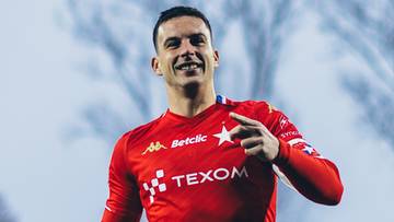 Piłkarz w czerwonej koszulce z numerem 9 i logo Texom biegnie po boisku stadionu.