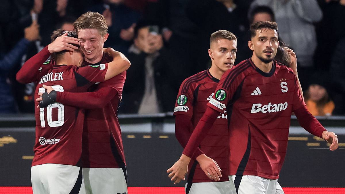 Piłkarze Sparty Praga celebrujący bramkę. W centrum kadru dw&oacute;ch zawodnik&oacute;w przytulających się na pierwszym planie, jeden z nich obejmuje drugiego za szyję. W tle widać innych piłkarzy i kibic&oacute;w.