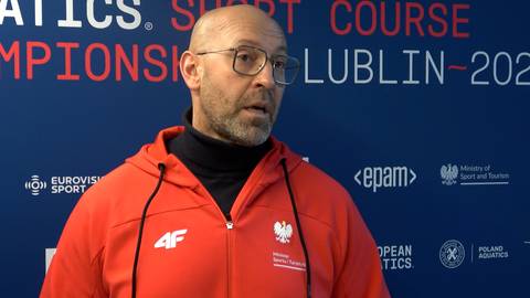 Mężczyzna w okularach i pomarańczowej bluzie z kapturem z godłem Polski, na tle z napisem "LUBLIN-2023".