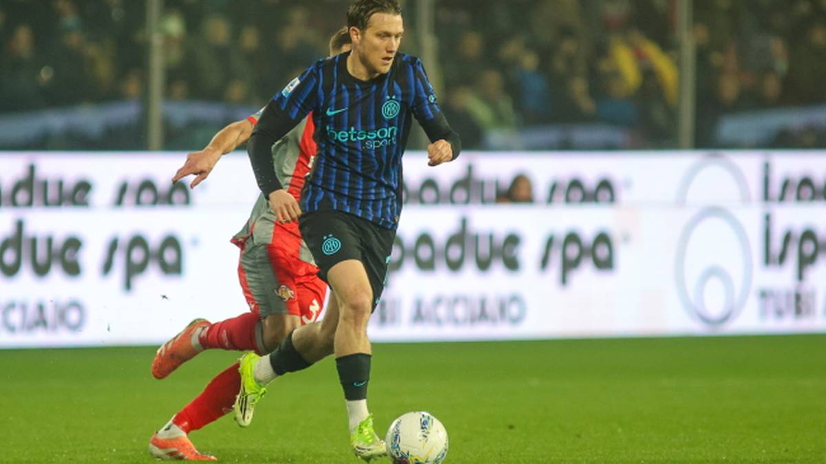 Piłkarz w czarno-niebieskiej koszulce Interu prowadzi piłkę po boisku, ścigany przez przeciwnika w czerwonym stroju.