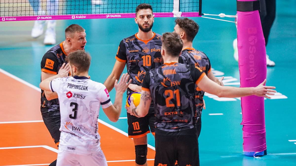 Grupa siatkarzy w strojach sportowych pozująca do zdjęcia na boisku.