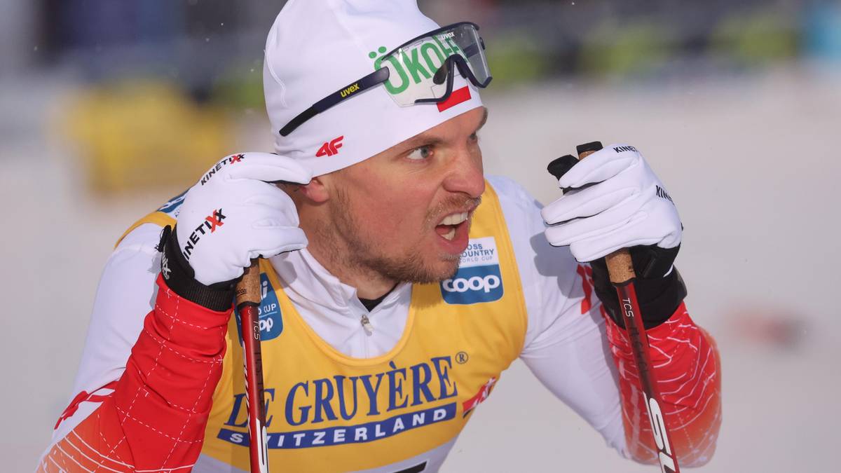 Narciarz biegowy Maciej Staręga w białej czapce i okularach, z numerem startowym 85 na piersi, trzymający kije narciarskie.