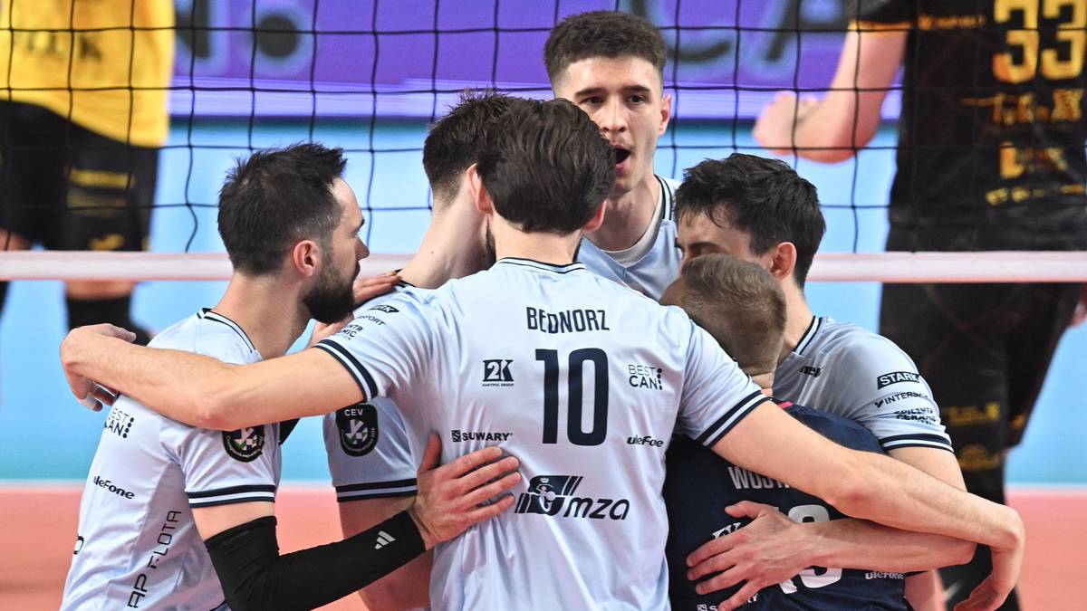 Siatkarze w geście radości i jedności, świętujący zdobycie punktu na boisku siatkarskim.