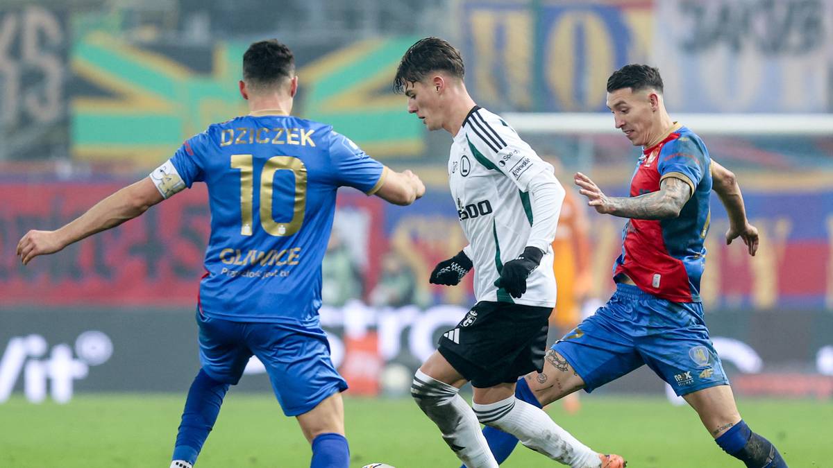 Piłkarze w białych i niebieskich strojach walczą o piłkę na boisku.