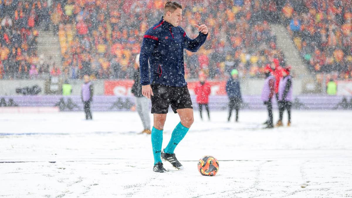 Piłkarz w granatowo-czerwonym stroju z piłką na zaśnieżonym boisku