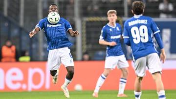 Piłkarz w niebieskim stroju z białymi spodenkami, uderza głową piłkę.