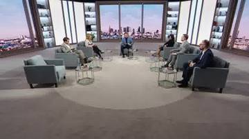 Ośmiu uczestników siedzi w fotelach w studiu telewizyjnym, dyskutując. W tle widok na miasto.