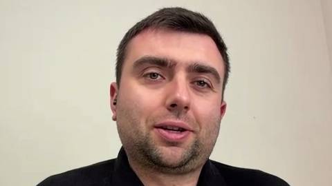 Portret mężczyzny o jasnej karnacji, kr&oacute;tkich ciemnych włosach i kilkudniowym zarostem, patrzącego w obiektyw i lekko się uśmiechającego.