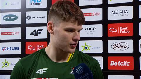 Młody mężczyzna w zielonej koszulce sportowej udziela wywiadu przed ścianą z logotypami sponsor&oacute;w.