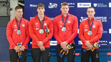 Czterech polskich pływaków w czerwonych bluzach i z medalami na szyjach stoi na podium.