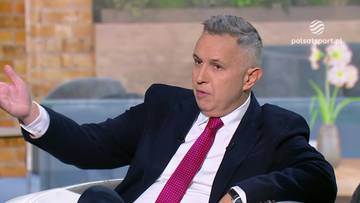 Mężczyzna w ciemnym garniturze i r&oacute;żowym krawacie siedzi i gestykuluje prawą ręką, rozmawiając. W tle widać wazon z kwiatami i logo Polsat Sport.