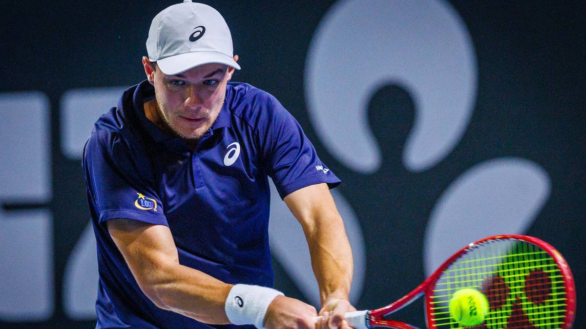 Tenisista w białej czapce i granatowej koszulce, wykonujący uderzenie forhendowe podczas meczu.