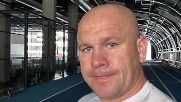 Łukasz Różański w białej koszulce z logo LOTTO, z płotkami lekkoatletycznymi w tle.