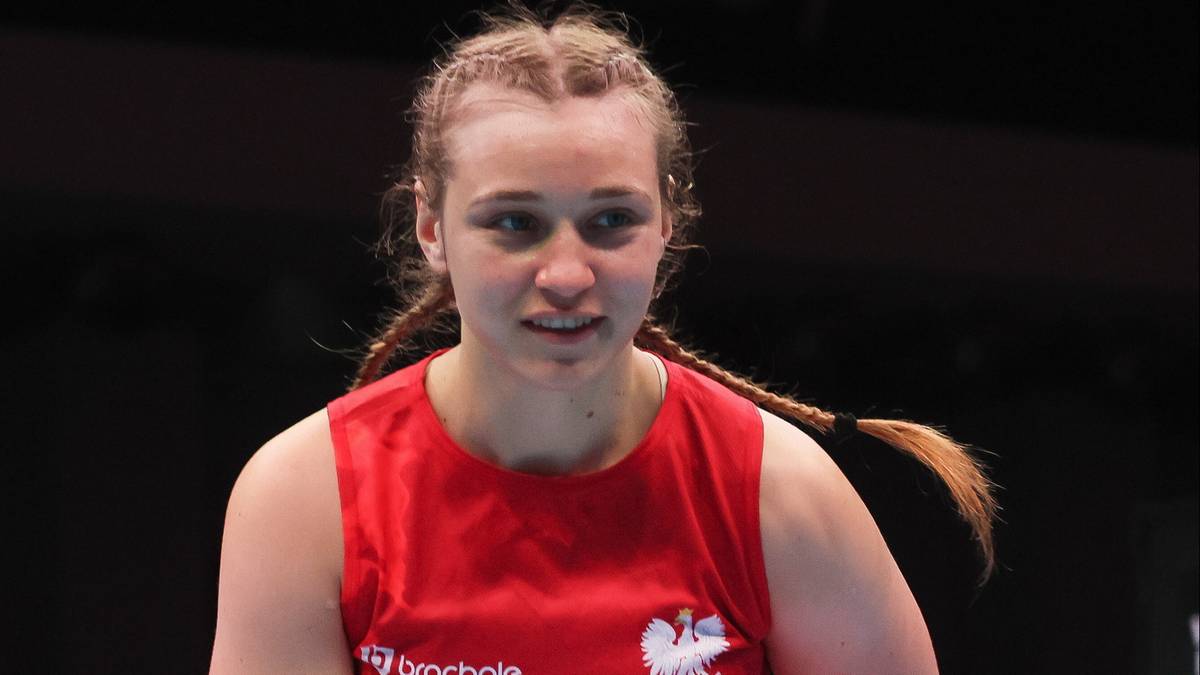 Młoda kobieta, zawodniczka boksu, z warkoczami, w czerwonej koszulce sportowej, patrzy przed siebie z determinacją.