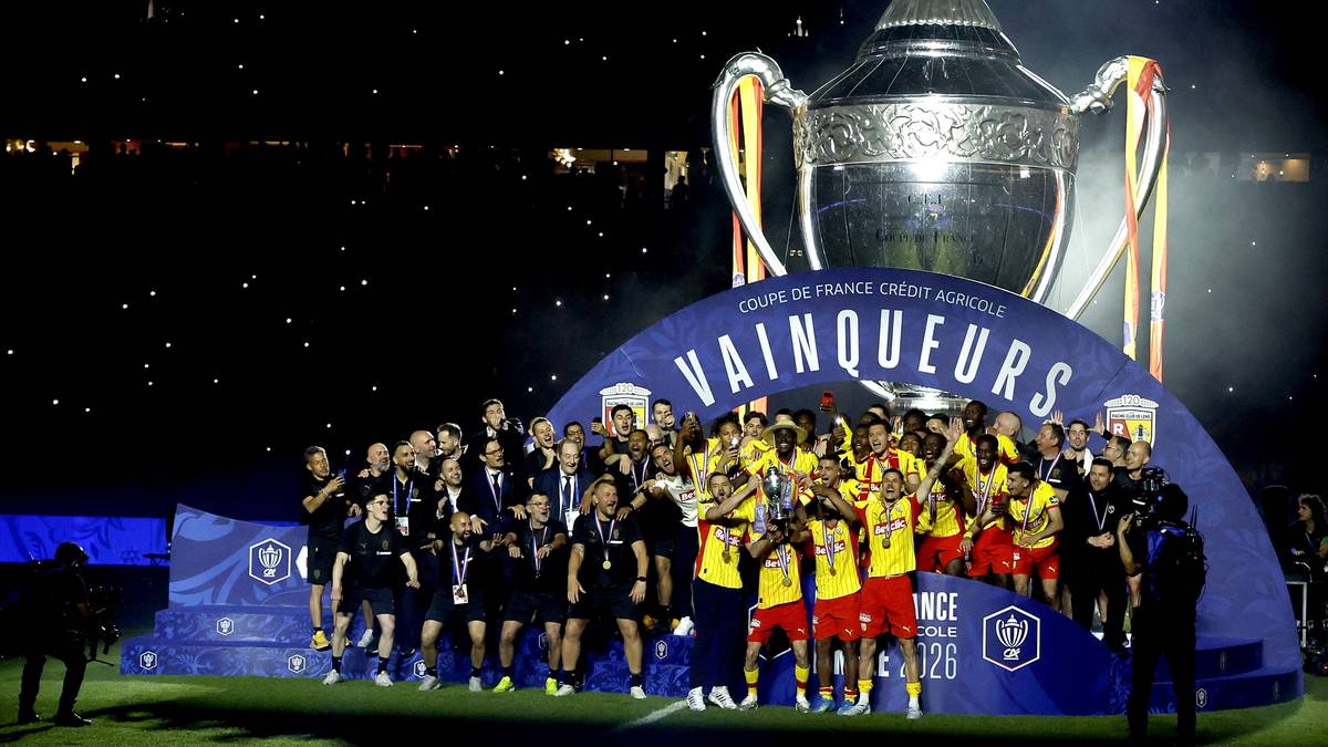 Drużyna piłkarska świętuje zdobycie trofeum na stadionie, z pucharem w tle.