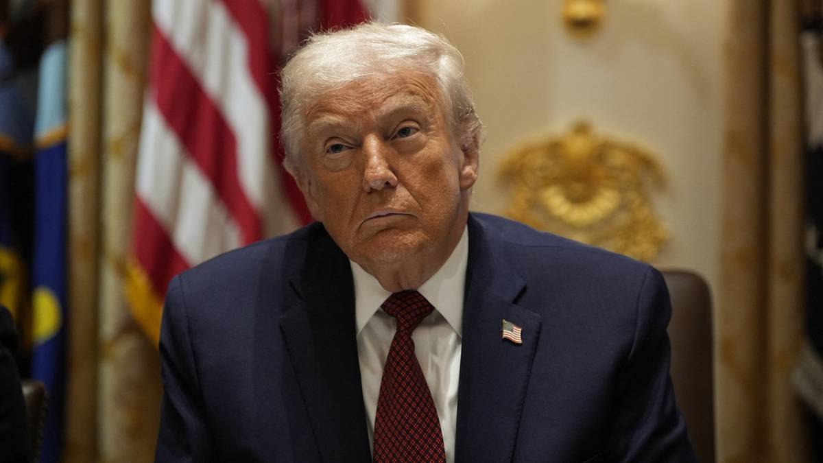 Donald Trump w gabinecie z amerykańską flagą w tle.