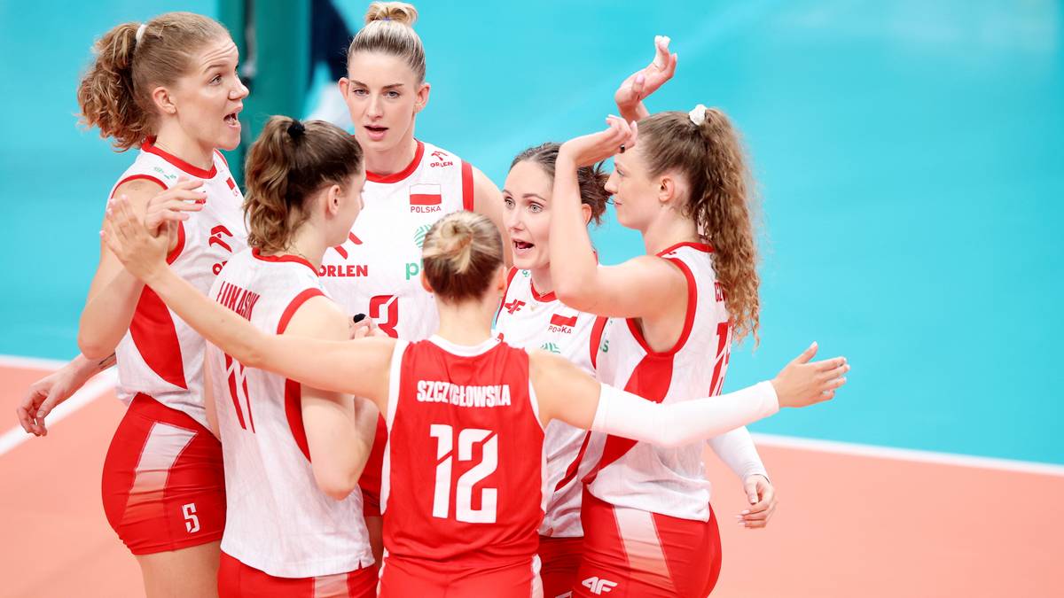 Grupa polskich siatkarek w czerwonych strojach sportowych, świętująca sukces lub omawiająca strategię.