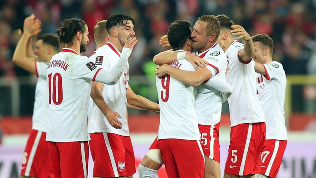 Piłkarze reprezentacji Polski w białych strojach z czerwonymi detalami, świętujący razem na boisku.