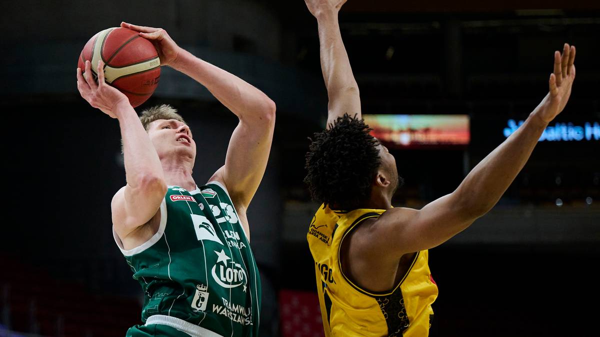 Koszykarz w zielonej koszulce z piłką w ręku oddaje rzut, a obok niego koszykarz w ż&oacute;łtej koszulce pr&oacute;buje go zablokować.