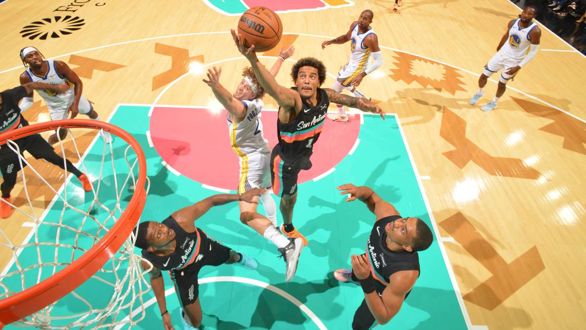 Gracze drużyny San Antonio Spurs w czarnych strojach rywalizują o piłkę z przeciwnikami w białych strojach podczas meczu koszykówki. Jeden z zawodników Spurs wykonuje rzut do kosza.