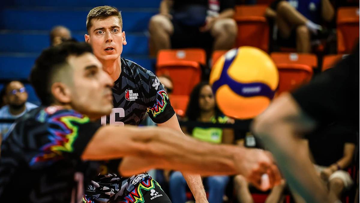 Siatkarz w czarno-kolorowym stroju z numerem 16 na plecach odbija piłkę, jego kolega z drużyny patrzy w kierunku piłki.