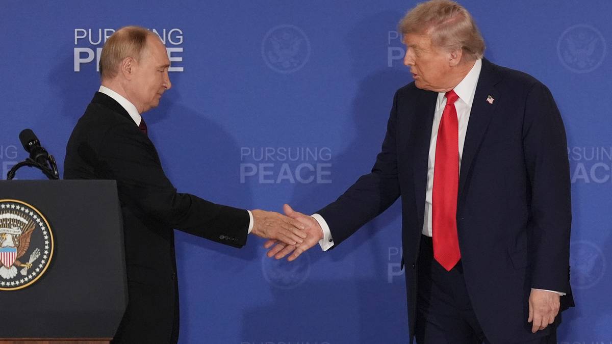 Donald Trump i Władimir Putin podają sobie ręce na tle niebieskiej ściany z napisem "PURSUING PEACE".